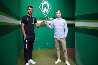 Dominik Kupilas (rechts im Bild) mit E-Sportler Fifabio (links); dahinter das Logo von Werder Bremen