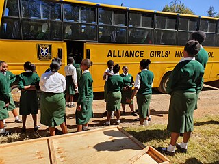 Ein gelber Schulbus mit der Aufschrift "Alliance Girls' High School", davor eine Gruppe von Schülerinnen