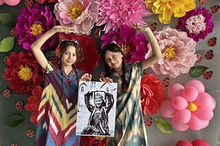Zwei junge Mädchen mit Krönchen auf dem Kopf stehen vor einer mit Luftballons, Marienkäfern und Papierblumen aufwändig dekorierten Wand.