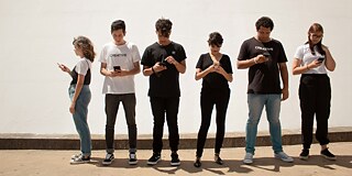 Sechs junge Menschen stehen nebeneinander und blicken konzentriert auf ihre Smartphones.