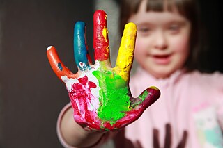 Mädchen mit Down-Syndrom hält ihre mit Farben bemalte Hand in die Kamera