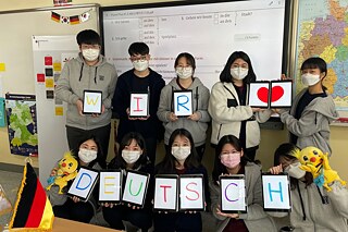 Gruppenfoto einer Klasse der SNU Oberschule mit deutscher und koreanischer Flagge im Klassenraum vor Deutschlandkarte