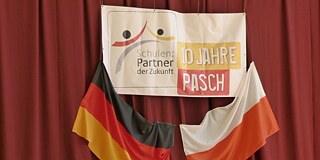 Deutsche und polnische Flagge mit PASCH-Banner vor einem Vorhang aufgehängt