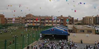 Schüler und Schülerinnen lassen Luftballons auf dem Sportplatz fliegen