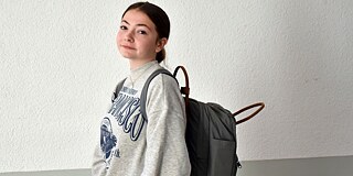 Marie-Sophie mit ihrem Schulrucksack vor einer weißen Wand, seitlich fotografiert