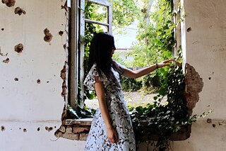 Mädchen in einem geblümten Kleid steht vor einem offenen Fenster