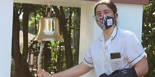 Schülerin läutet eine goldene Glocke im Außenbereich der Schule