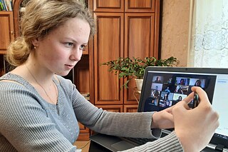 Schülerin sitzt an ihrem Schreibtisch vor ihrem aufgeklappten Laptop und fotografiert sich selbst mit ihrem Handy