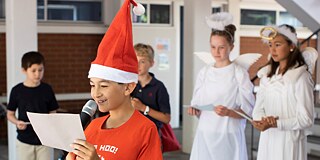 Verkleidete Schüler und Schülerinnen, im Vordergrund ein Schüler mit Weihnachtsmütze, der einen Text vorliest