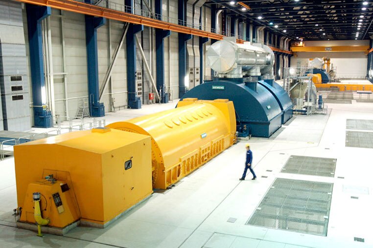 Mann in Schutzkleidung geht in einem Kraftwerk zu einem gelben Generator