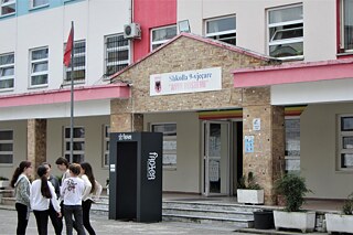 Gebäude von außen, mehrere Schüler und Schülerinnen stehen in einem kleinen Kreis vor dem Gebäude