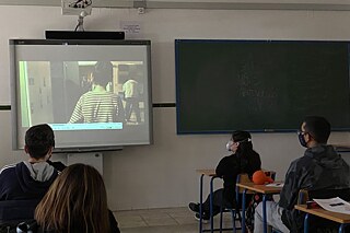 Schüler und Schülerinnen sitzen mit Masken an ihren Tischen und schauen Film