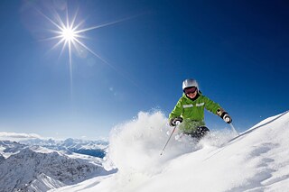 Skifahrer in grüner Jacke wirbelt Schnee auf