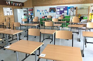 Leeres Klassenzimmer mit hochgestellten Stühlen und Plakaten an den Wänden