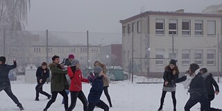 Schüler und Schülerinnen bewerfen sich vor dem Schulgebäude mit Schneebällen