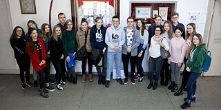Schüler und Schülerinnen stehen für ein Gruppenfoto zusammen auf dem Schulflur vor der PASCH-Plakette an der Wand.