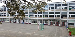 Weißes Schulgebäude mit Fussballplatz im Vordergrund