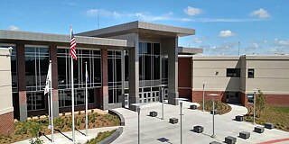 Aufnahme des Schulgebäudes von oben, Blick auf den verglasten Hauseingang mit USA-Flagge vor dem Eingang