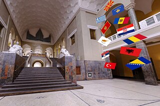 Innenbereich der Ludwig-Maximilians-Universität München mit Blick auf eine Treppe, daneben verschiedene Länderflaggen, die eingeblendet werden