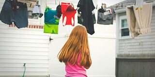 Kleider-Geschichten Britanny Colette © Unsplash Mädchen mit pinkem Oberteil steht vor einer Wäscheleine, mit dem Rücken zur Kamera