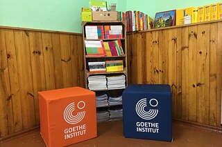 Ein orangener und ein dunkelblauer Hocker des Goethe-Instituts in einer Leseecke