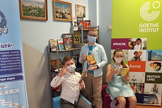 Drei Schulkinder mit Masken halten deutsche Rezeptbücher in die Kamera