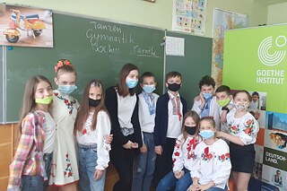 Schüler und Schülerinnen vor einer Tafel in der Schule in traditioneller Kleidung mit Blumenkränzen