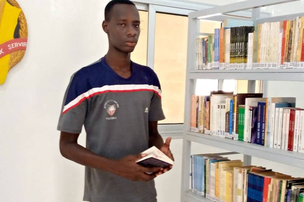 Ein Mann steht vor einem Bücherregal und hält ein Buch in den Händen