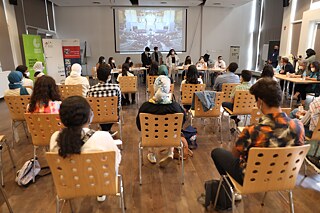 Schülerinnen und Schüler sitzen auf Holzstühlen