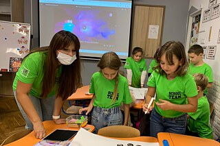 Schülerinnen und Schüler in den gleichen grünen T-Shirts stehen an einem Tisch und besprechen sich