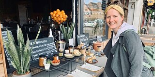 Betty Wilde ist Contentmanagerin beim Reiseanbieter FairAway © privat Frau steht vor einem Cafe und lächelt in die Kamera