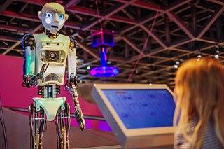 Ein Mädchen steht vor einem Display und einem großen Roboter