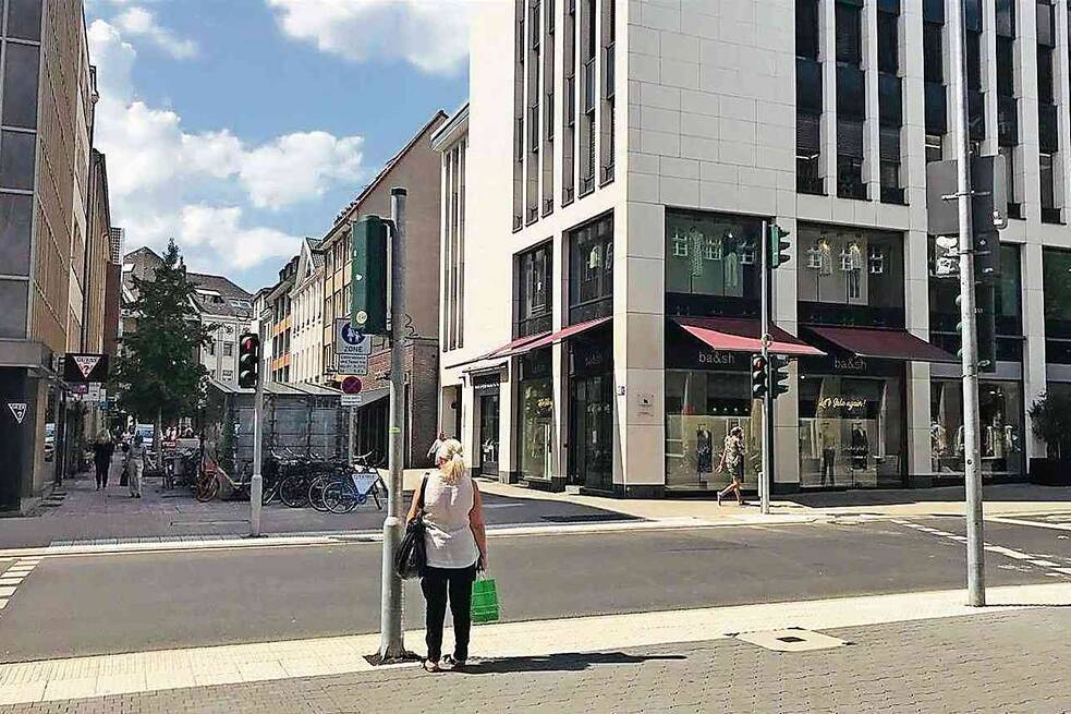 Straße in der Innenstadt, eine Frau steht an einer Ampel