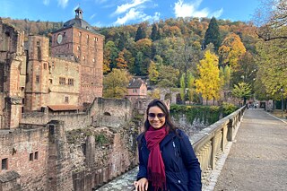 Larissa in schwarzer Jacke und mit einem roten Schal und einer Sonnenbrille vor dem Heidelberger Schloss