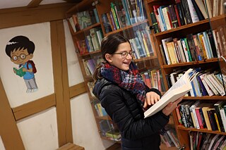 Lisa steht vor einem Bücherregal und hält ein aufgeklapptes Buch in der Hand