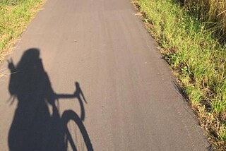 Schatten eines Mädchens, das auf einem Fahrrad sitzt und auf einem Weg neben einem Feld fährt