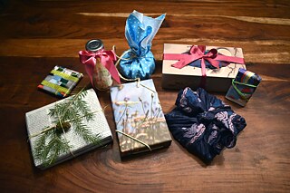 Aufwändig und bunt verpackte Geschenke auf einem dunklen Holztisch, von oben fotografiert