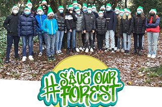 Schülerinnen und Schüler stehen mit grünen Weihnachtsmützen zusammen für ein Gruppenbild im Wald. Darunter das Logo zu #saveourforest