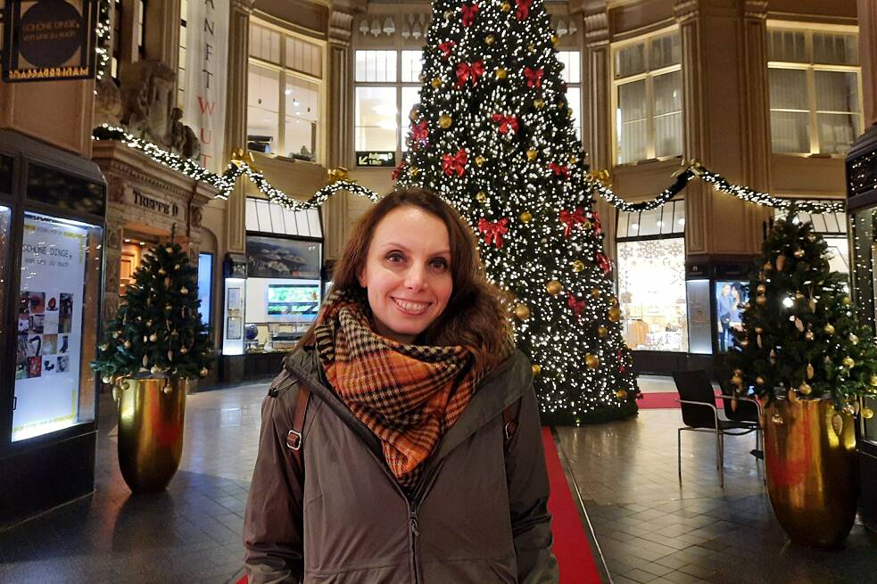 Foto einer Frau in einem Einkaufszentrum, im Hintergrund ein festlich geschmückter großer Weihnachtsbaum