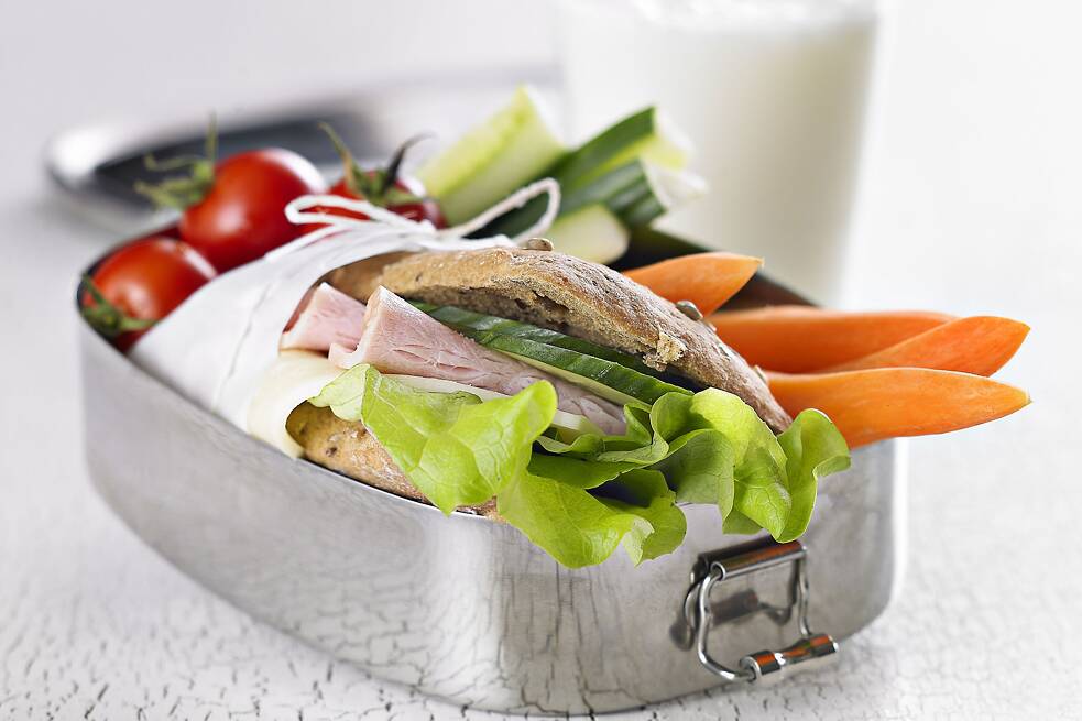 Brotdose aus Metall, gefüllt mit Brot, geschnittenen Möhren, Gurken, Tomaten und Salat
