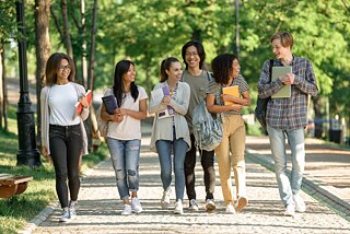 Schülerinnen und Schüler laufen zusammen mit ihren Schulbüchern über einen Weg, im Hintergrund Bäume