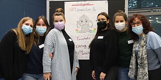 Sechs Frauen mit Mund-Nasen-Schutz vor einem beschriebenen Flipboard