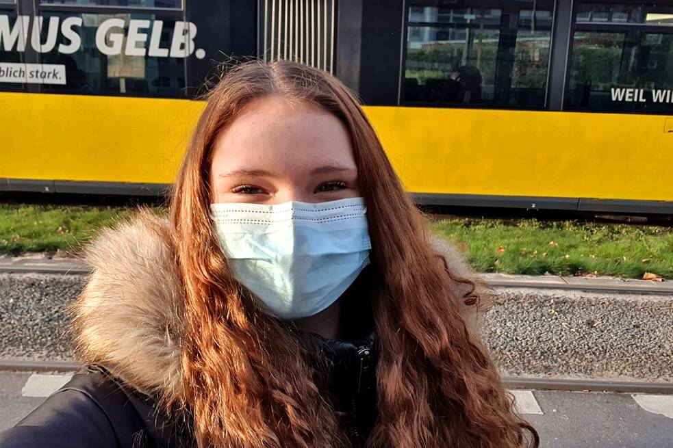 Ise mit OP-Maske vor einer gelben Straßenbahn