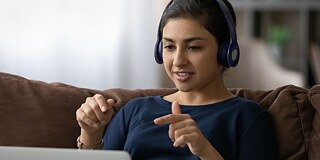 Eine Frau sitzt mit Headset vor Ihrem Laptop und gestikuliert mit den Händen