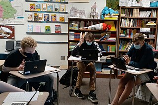 Drei Jugendliche sitzen an Einzeltischen vor ihren Laptops und konzentrieren sich