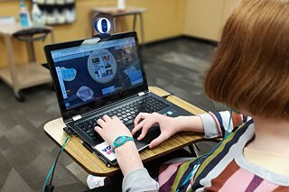 Frau mit roten Haaren und einem bunten Pullover schaut auf ihren Laptop