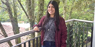 Sara Chica aus Kolumbien © privat Eine Frau mit langen Haaren und einer dunkelroten Jacke steht auf einem Balkon und lächelt in die Kamera