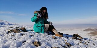 Frau in türkiser Winterjacke und Stiefeln auf einem verschneiten Berg
