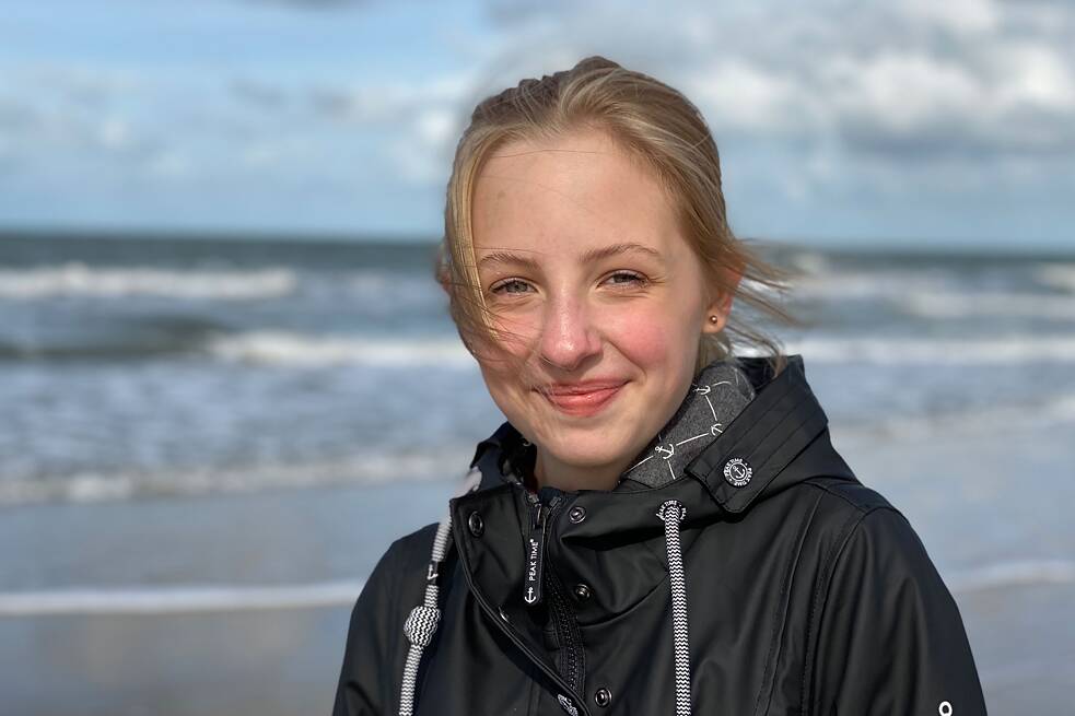 Jugendliche in schwarzer Windjacke am Meer fotografiert