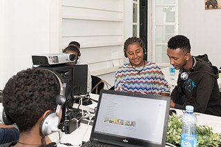Mehrere Jugendliche sitzen an einem Tisch und arbeiten an Laptops
